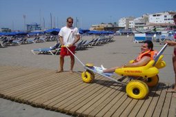 A volunteer who helps out a handicapped in amphibian chair to reach the seashore.